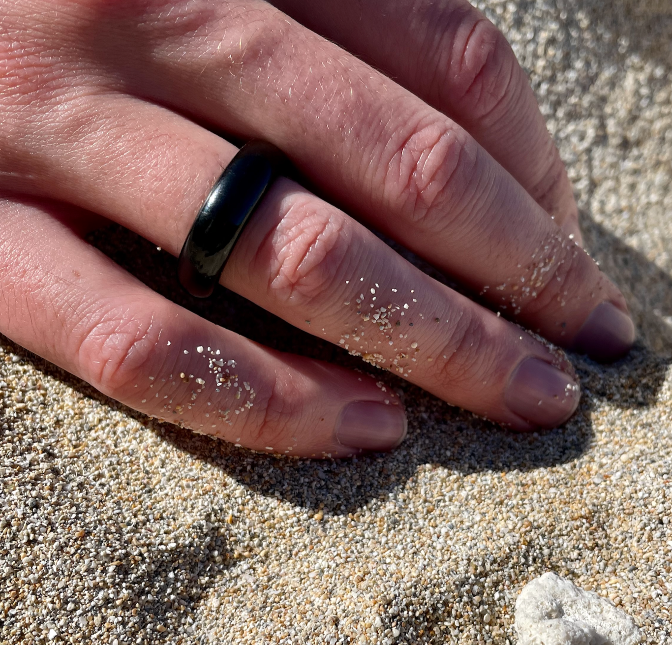 black onyx ring on man's hand resting on beach sand, by whitestone jewelry co.