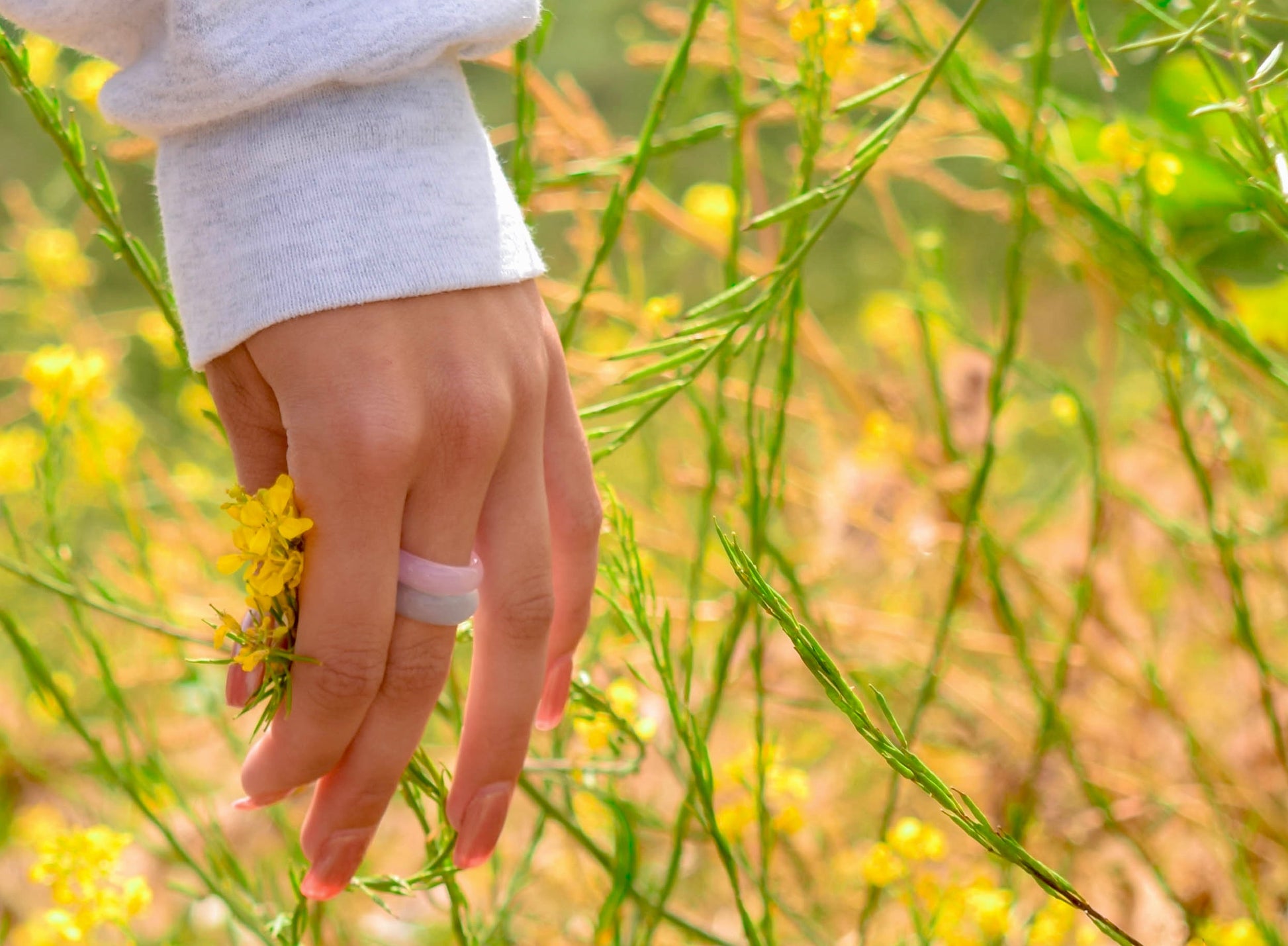 pink agate and blue agate rings paired together on a woman's hand, holding yellow flowers, by whitestone jewelry co.