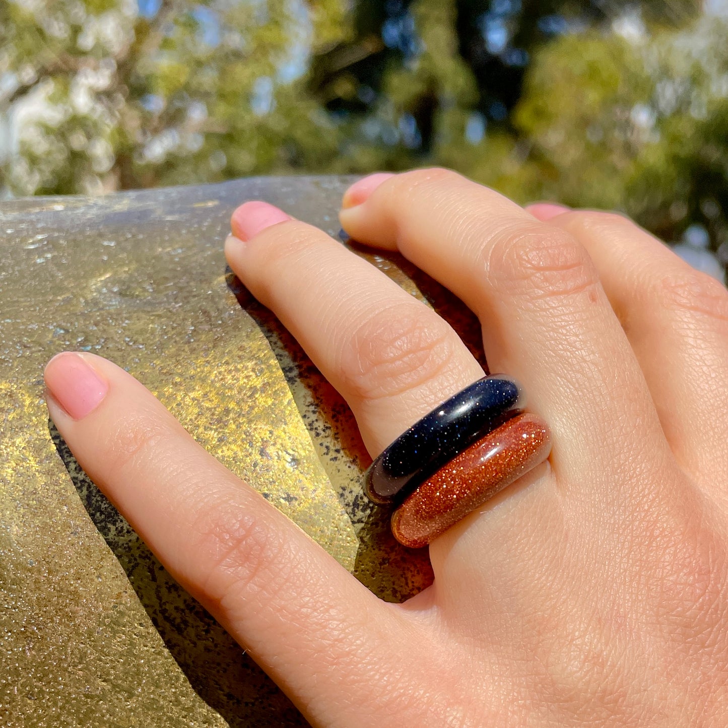 blue sandstone and goldstone rings paired together on a woman's hand, resting on a bronze sculpture, by whitestone jewelry co.