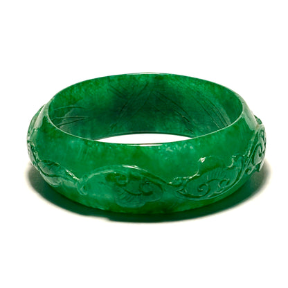 Green jade bracelet with intricate carvings on a white background