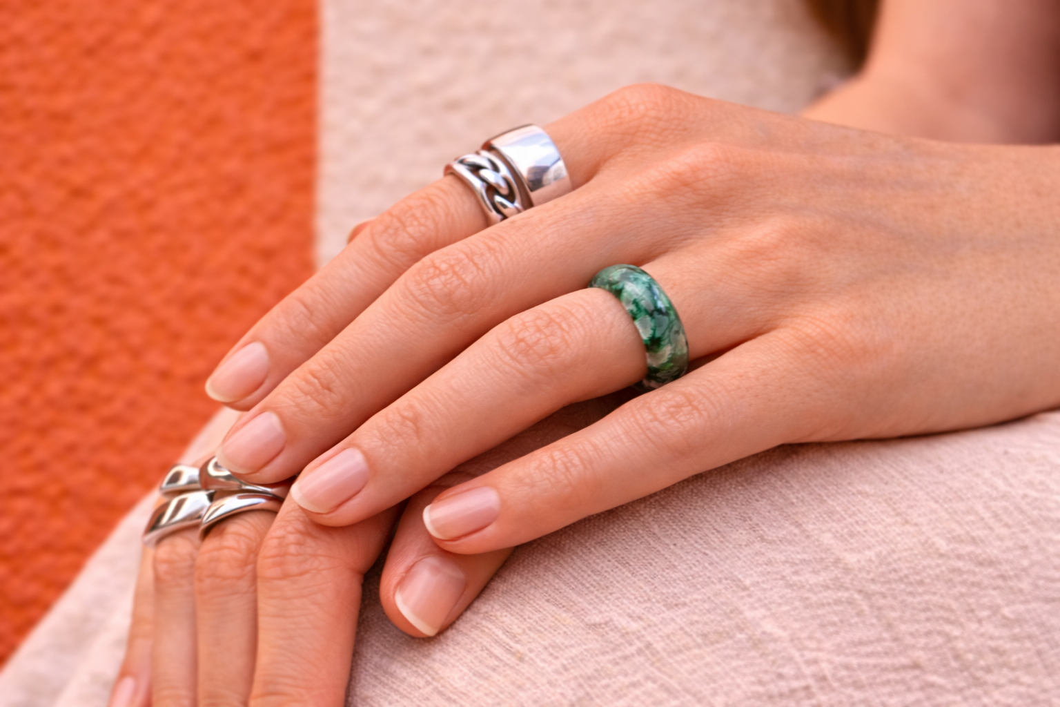 Close-up of hands with silver and green rings on a textured surface