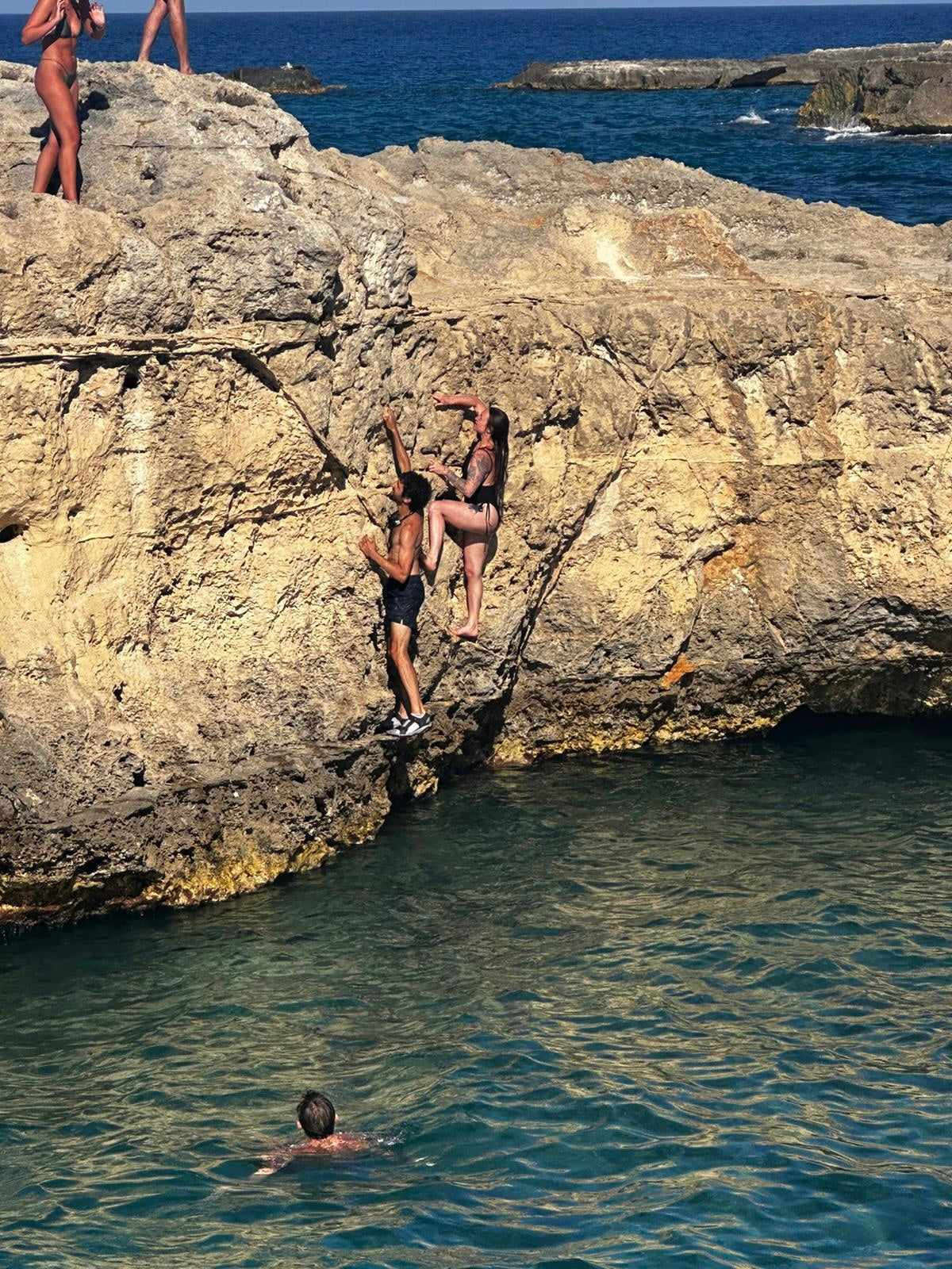 Two people climbing a rocky cliff above the sea in the Puglia region of Italy.