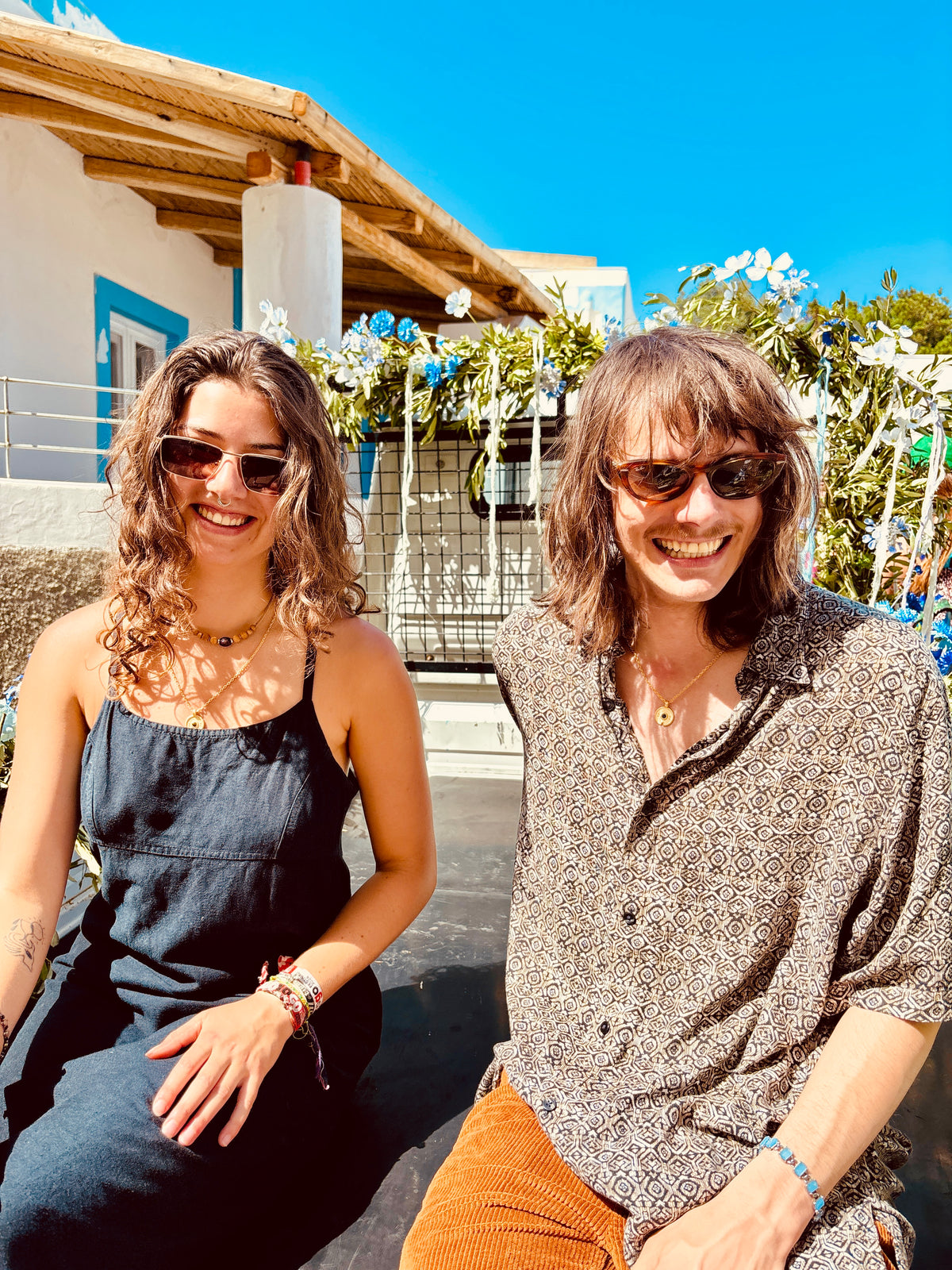 a man and women wearing the nura pendant necklace while sitting outdoors smiling on Lipari island off the coast of Sicily. 
