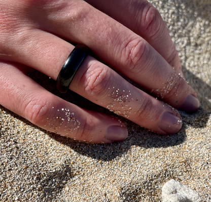 black onyx ring on man's hand resting on beach sand, by whitestone jewelry co.